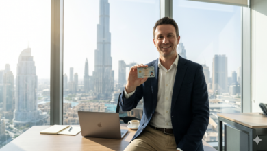 A natural, candid photo of a successful international professional holding a UAE residency card in a modern glass office in Downtown Dubai, with the Burj Khalifa and skyline in the background.