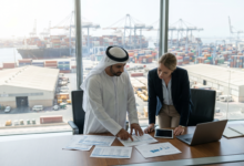 Corporate executives reviewing shipping documents and logistics plans inside a modern office overlooking the container terminals at Jebel Ali Free Zone (JAFZA) in Dubai.